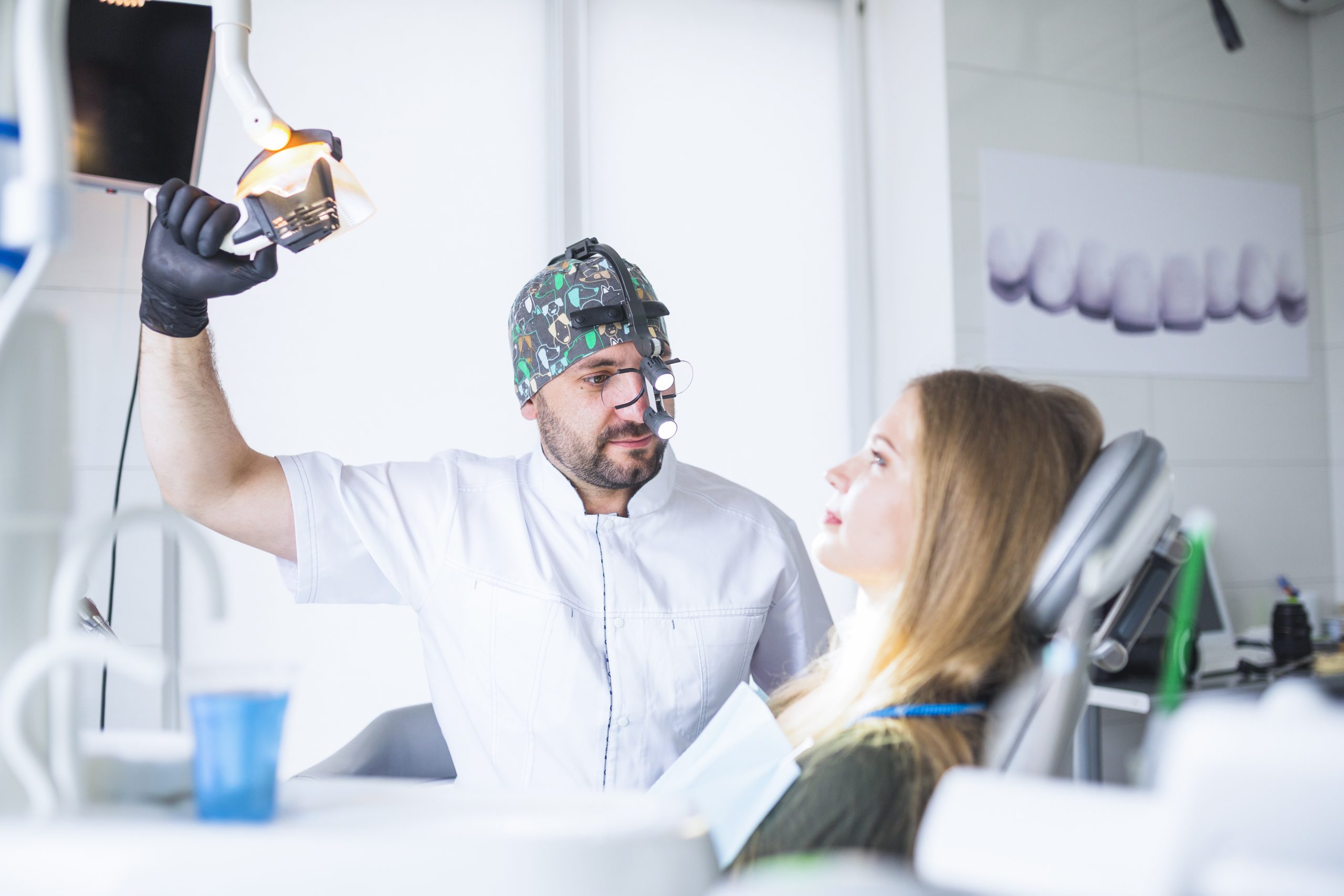 a man in a white coat and hat - a dentist examining a female patient