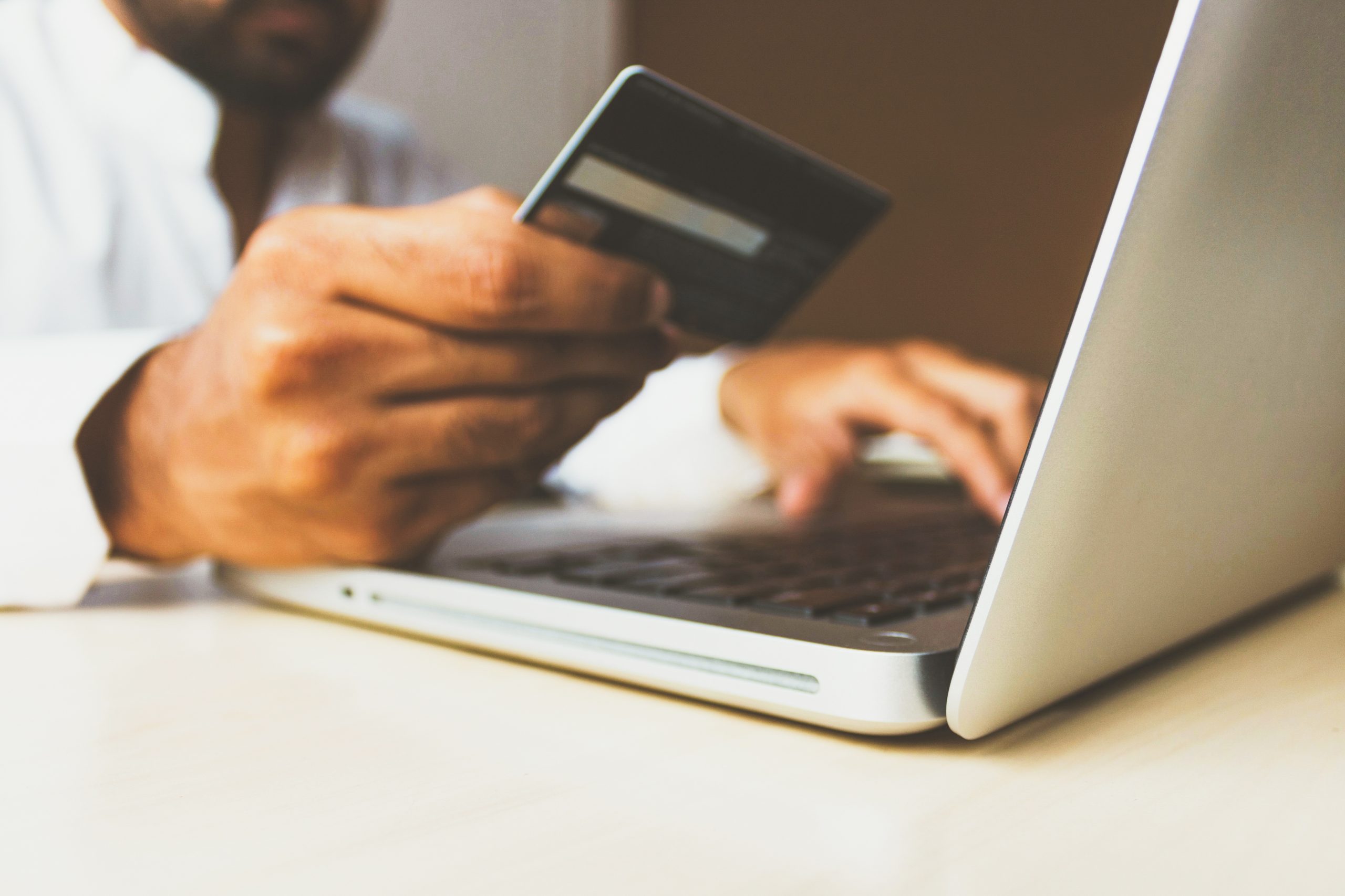 a close up of hands holding a credit card and a laptop on a table
