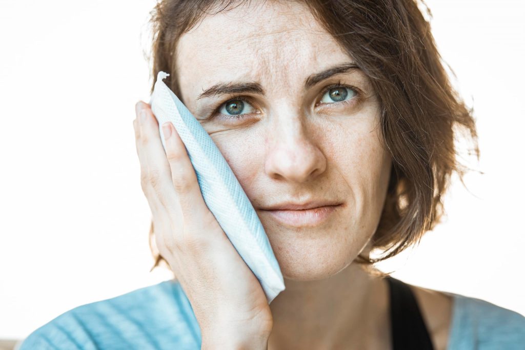 a woman in pain holding a hot compress towel on her cheek