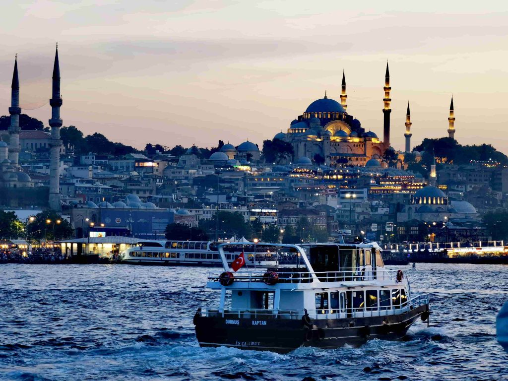 Evening across the Bosphorus: a ferry glides past the illuminated Suleymaniye Mosque and the minaret-studded skyline of Istanbul