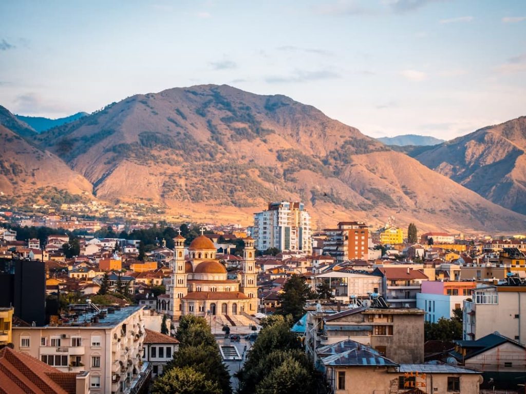 Albanian city skyline with church and mountain backdrop at sunset—affordable dental tourism destination for Italians seeking implants and veneers.